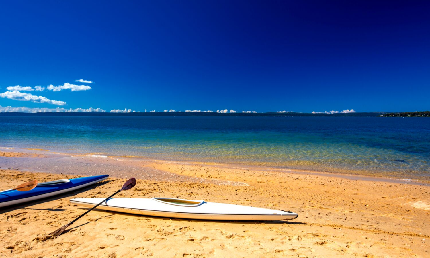 Beach scene with kayaks in the forefront. Rich blue sky and clear blue water. 